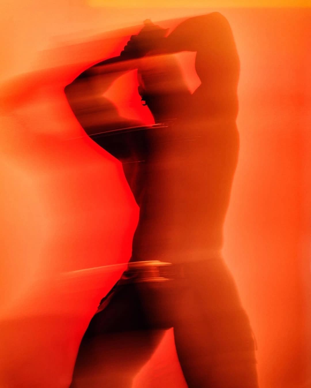 Abstrakte Bewegungsstudie einer tanzenden Person in warmem orangefarbenem Licht.